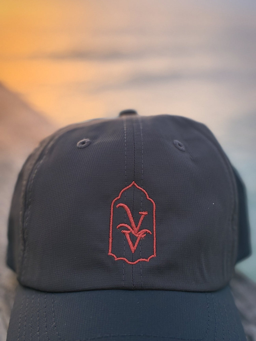 Close-up of the coral VV embroidery on the Venice Vida Afterglow Hat in Dark Grey against a golden sunset