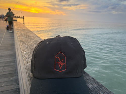 Venice Vida Afterglow Hat in Dark Grey with coral embroidered VV mark on the Venice Fishing Pier at sunset over the Gulf