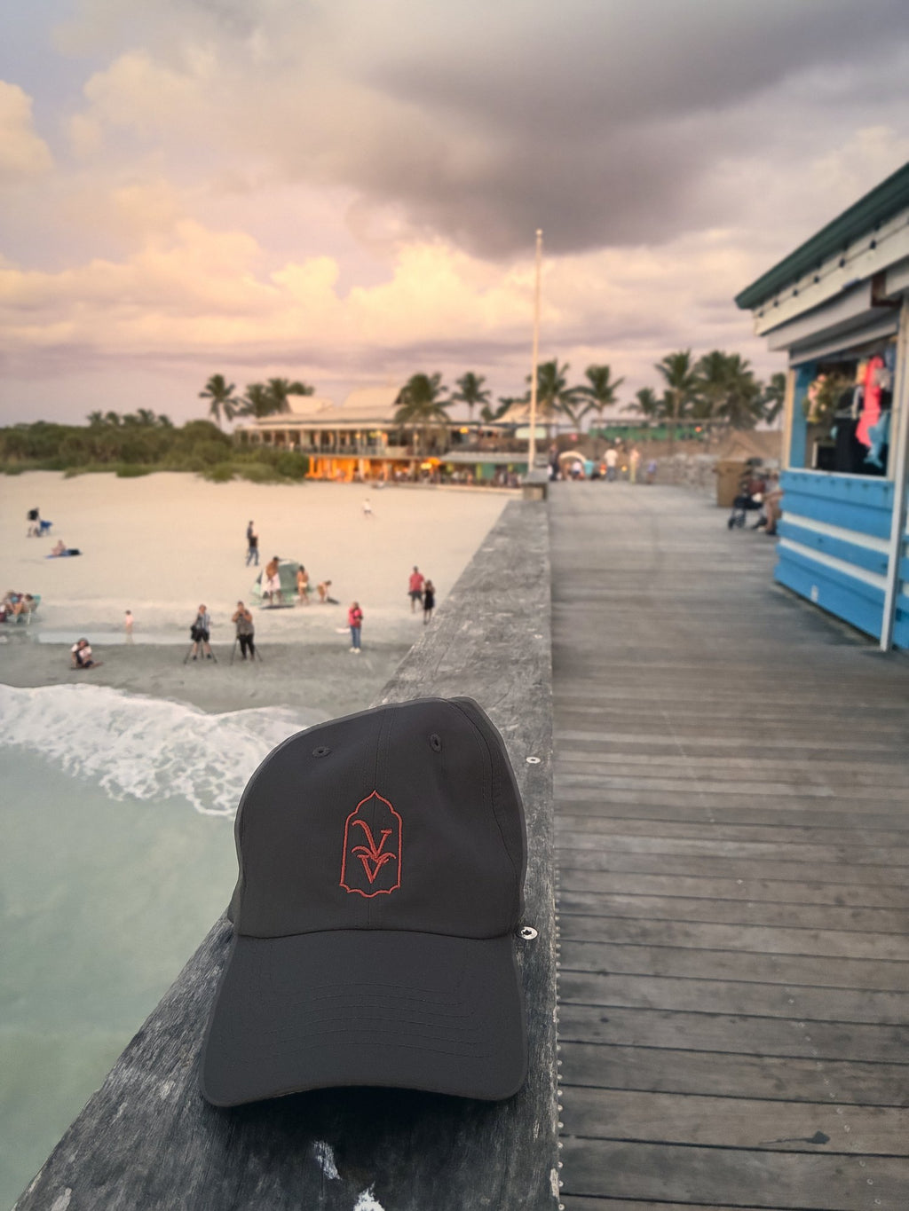Venice Vida Afterglow Hat in Dark Grey on the Venice Fishing Pier railing above the beach in Venice, Florida