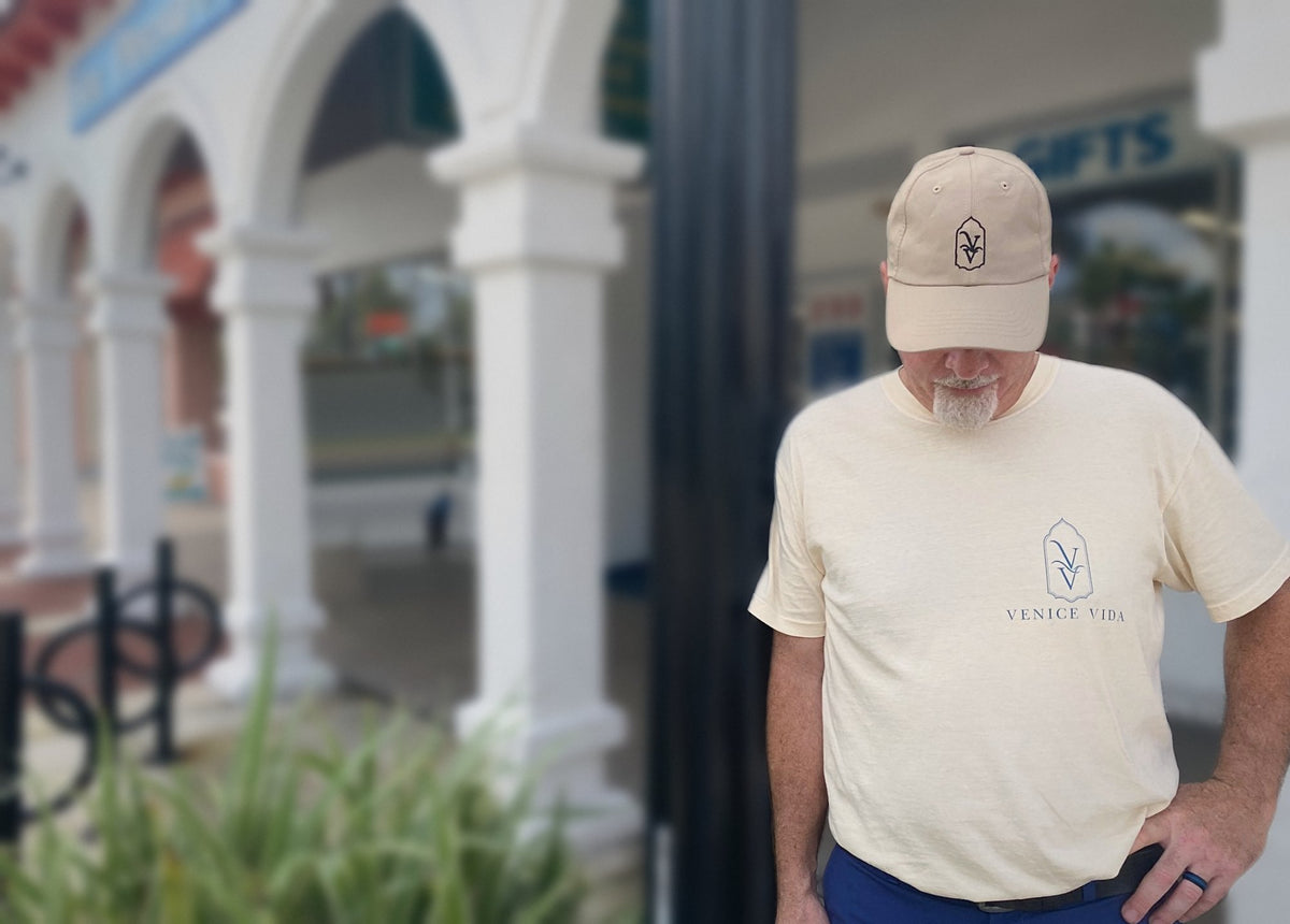 Venice Vida co-founder wearing the Mediterranean Heritage Tee in Ivory and Whitewash Hat beneath the Mediterranean arches of downtown Venice, Florida