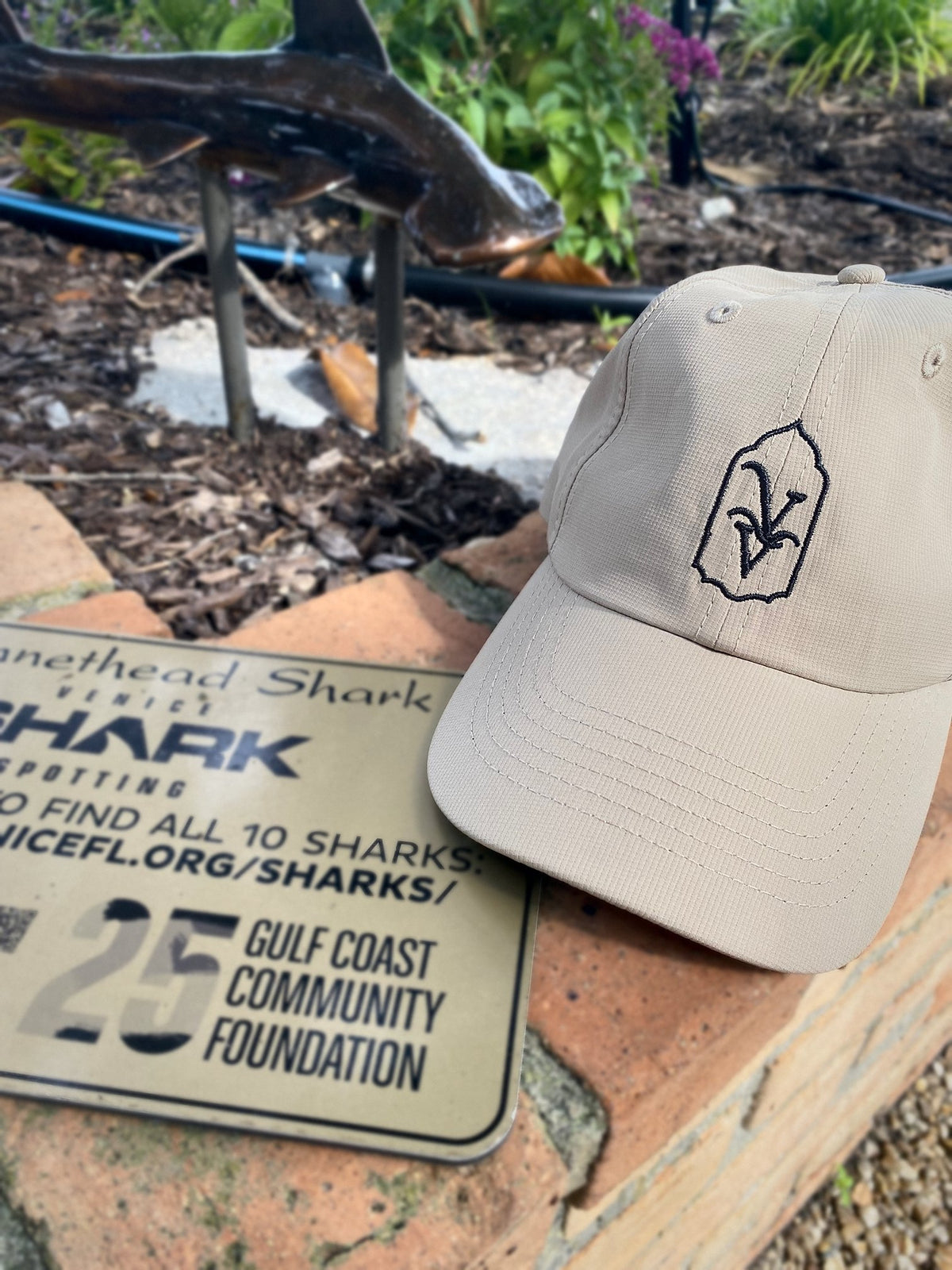 Venice Vida Heritage Hat in Khaki, close-up of the embroidered VV mark beside a Venice shark sculpture