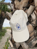 Venice Vida Whitewash Hat in Macaroon with royal blue embroidered VV mark on a palm tree by the beach in Venice, Florida