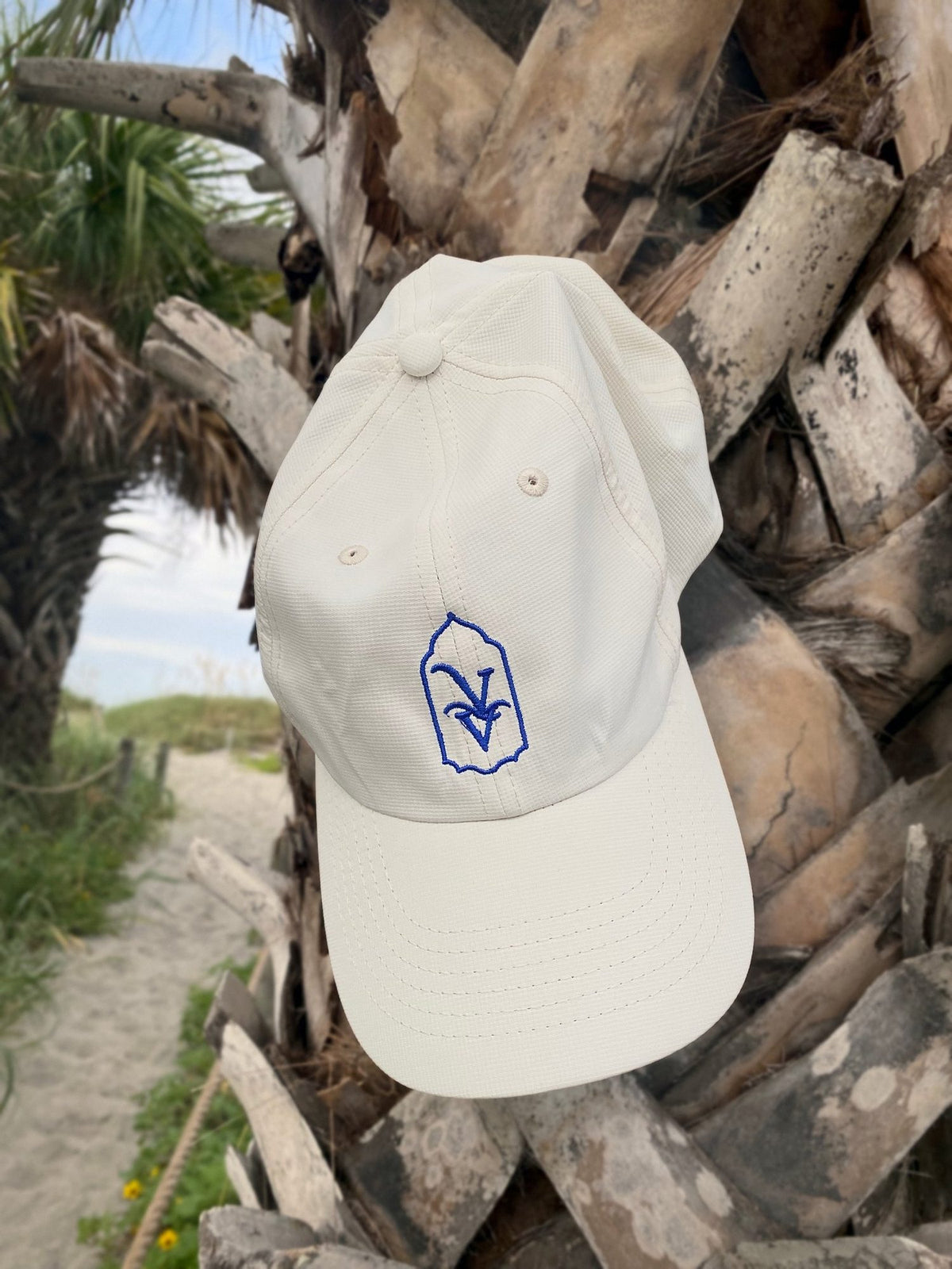 Venice Vida Whitewash Hat in Macaroon with royal blue embroidered VV mark on a palm tree by the beach in Venice, Florida