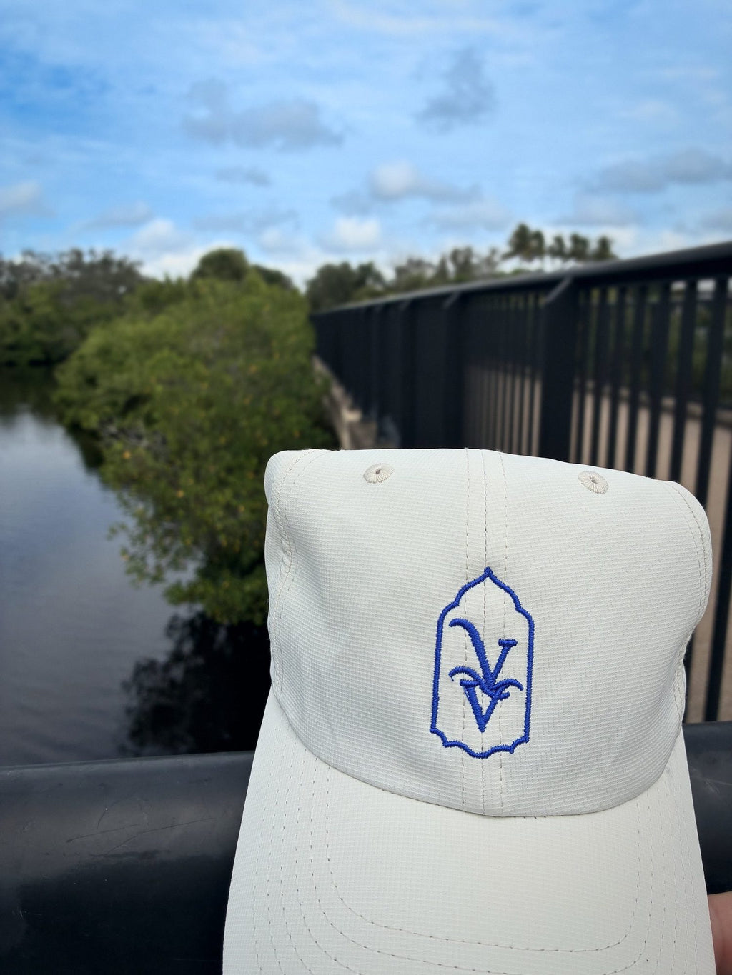 Close-up of the royal blue VV embroidery on the Venice Vida Whitewash Hat in Macaroon, on a bridge over the water in Venice, Florida