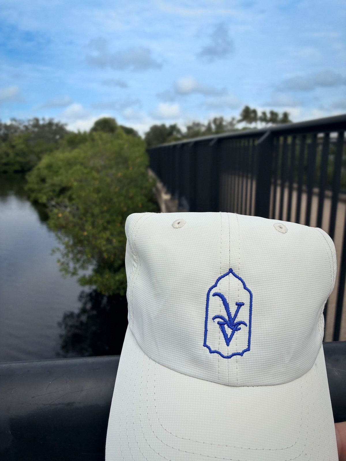 Close-up of the royal blue VV embroidery on the Venice Vida Whitewash Hat in Macaroon, on a bridge over the water in Venice, Florida
